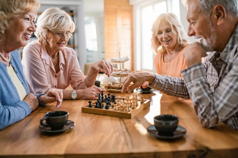 Happy mature friends enjoying while playing chess during coffee time at home.